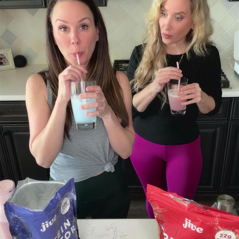 Two women sipping Protein Hydrator through straws in their kitchen