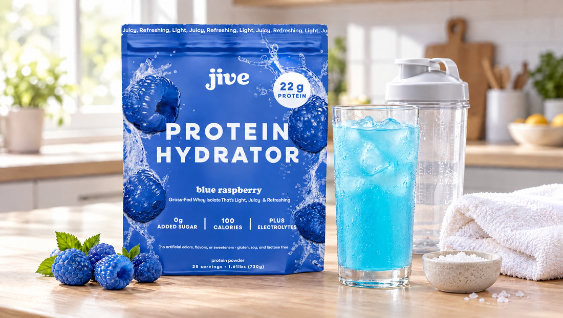 Jive Protein Hydrator Blue Raspberry pouch next to a glass of clear blue protein drink over ice, a shaker bottle and a gym towel