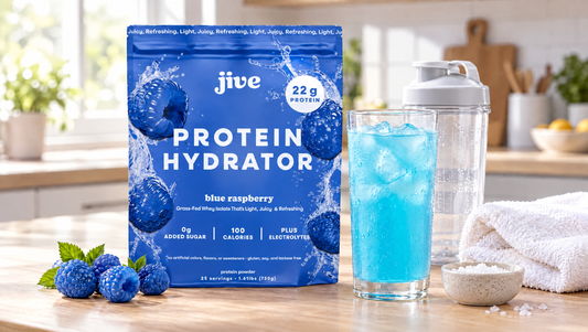 Jive Protein Hydrator Blue Raspberry pouch next to a glass of clear blue protein drink over ice, a shaker bottle and a gym towel