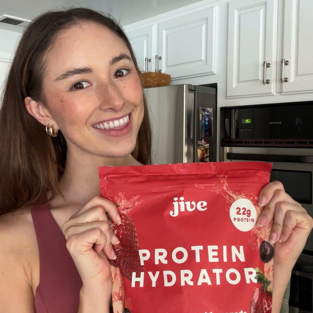 A smiling woman holding a bag of Strawberry Acai Lemonade Protein Hydrator