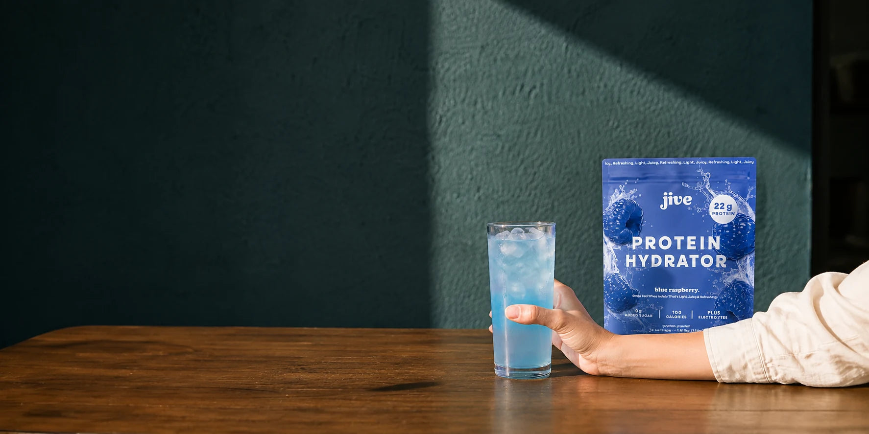 Jive Blue Raspberry Protein Hydrator beside an iced drink, held at a sunlit table